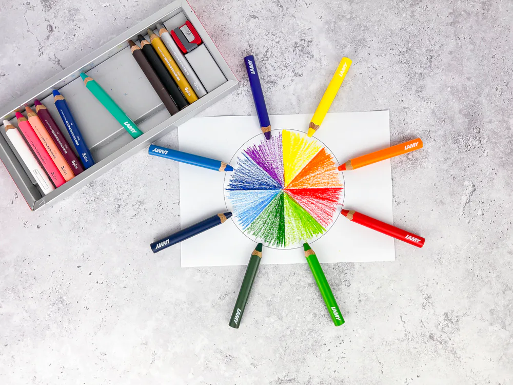 LAMY 3plus Farbstifte im Kreis um einen ausgemalten Farbkreis, daneben die Verpackung