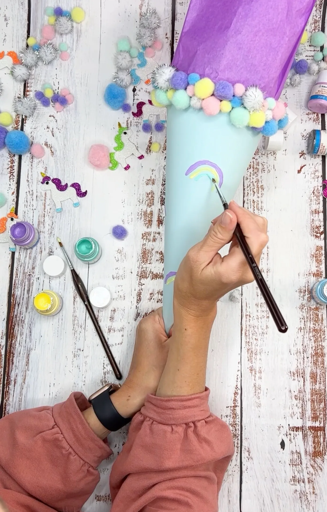 Ein kleiner Regenbogen wird mit dem Pinsel auf die Schultüte gemalt