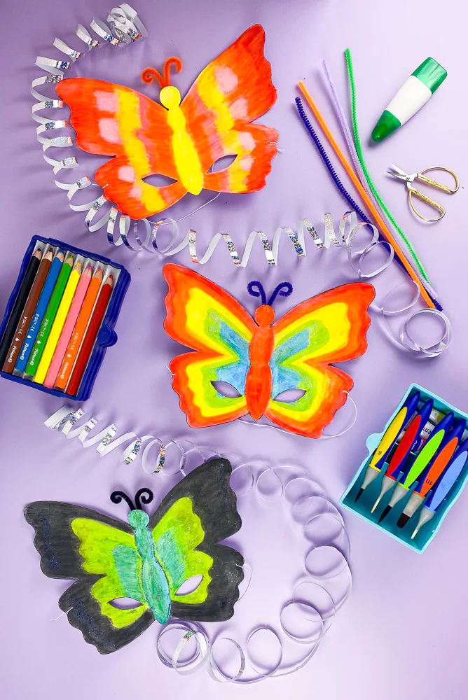 Drei bunt bemalte Schmetterlingsmasken aus Papier mit Bastelmaterial