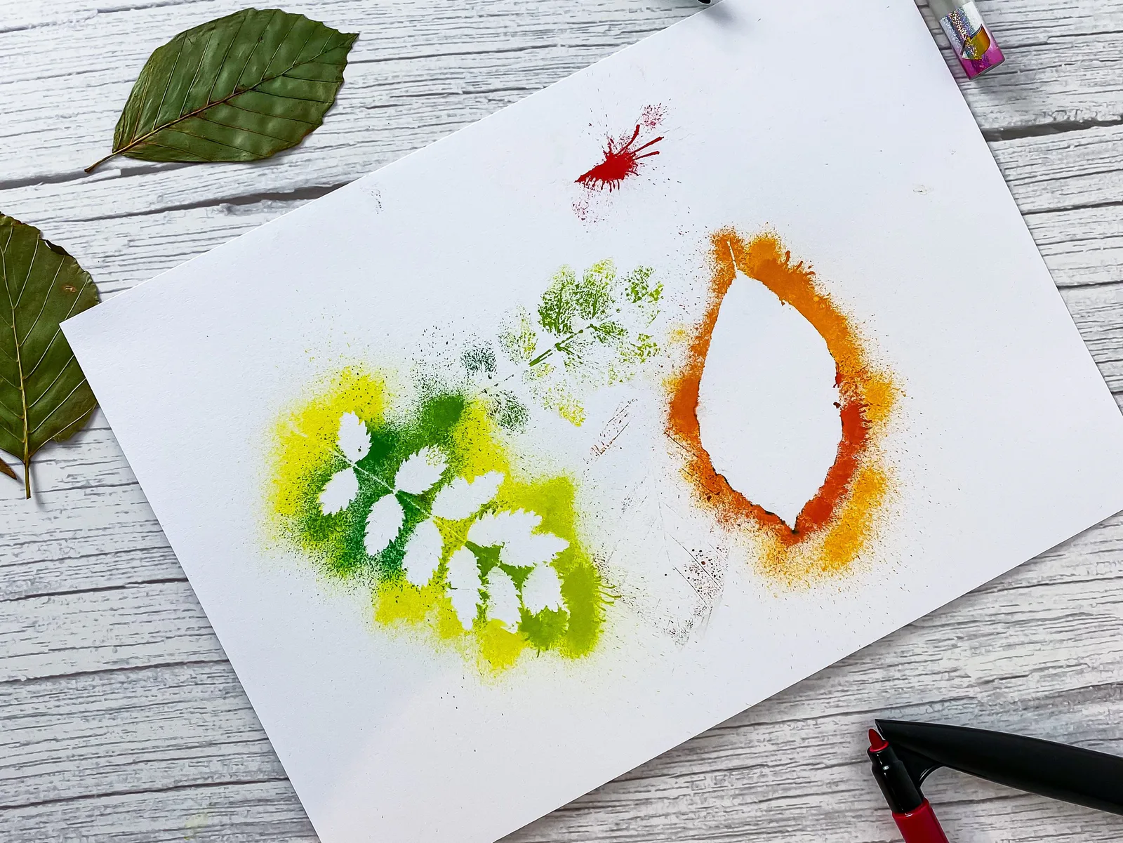 Gepustete Blattumrisse in Gelb, Grün und Orange auf weißem Papier