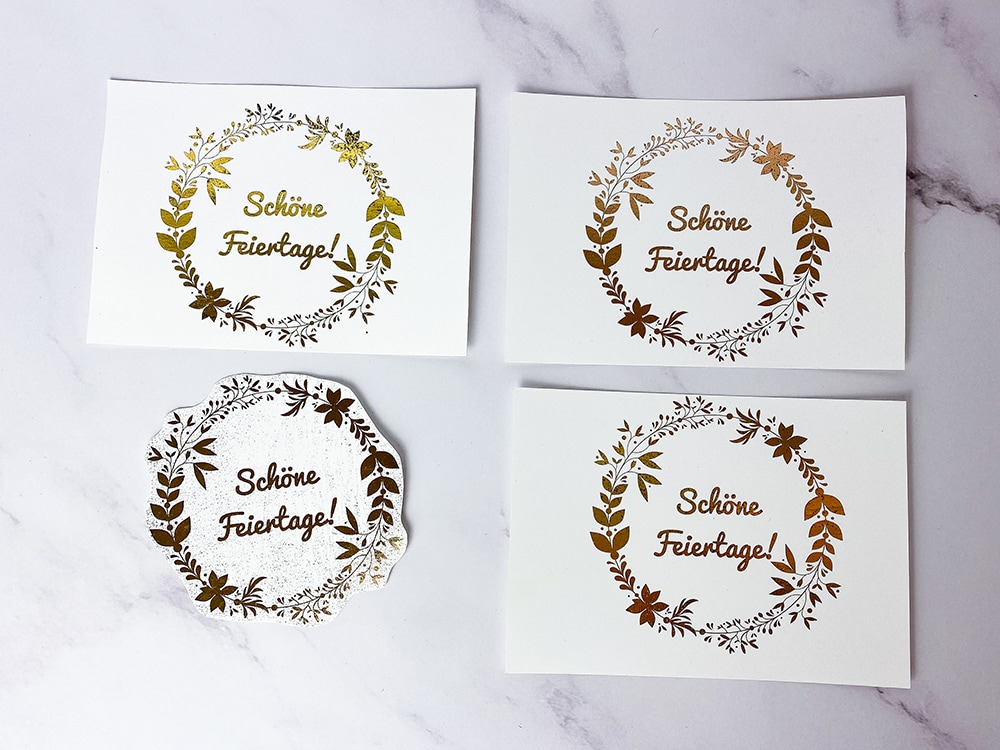 Karten mit dem Schriftzug Schöne Feiertage und Blumenkranz in verschiedenen Metallic-Farben