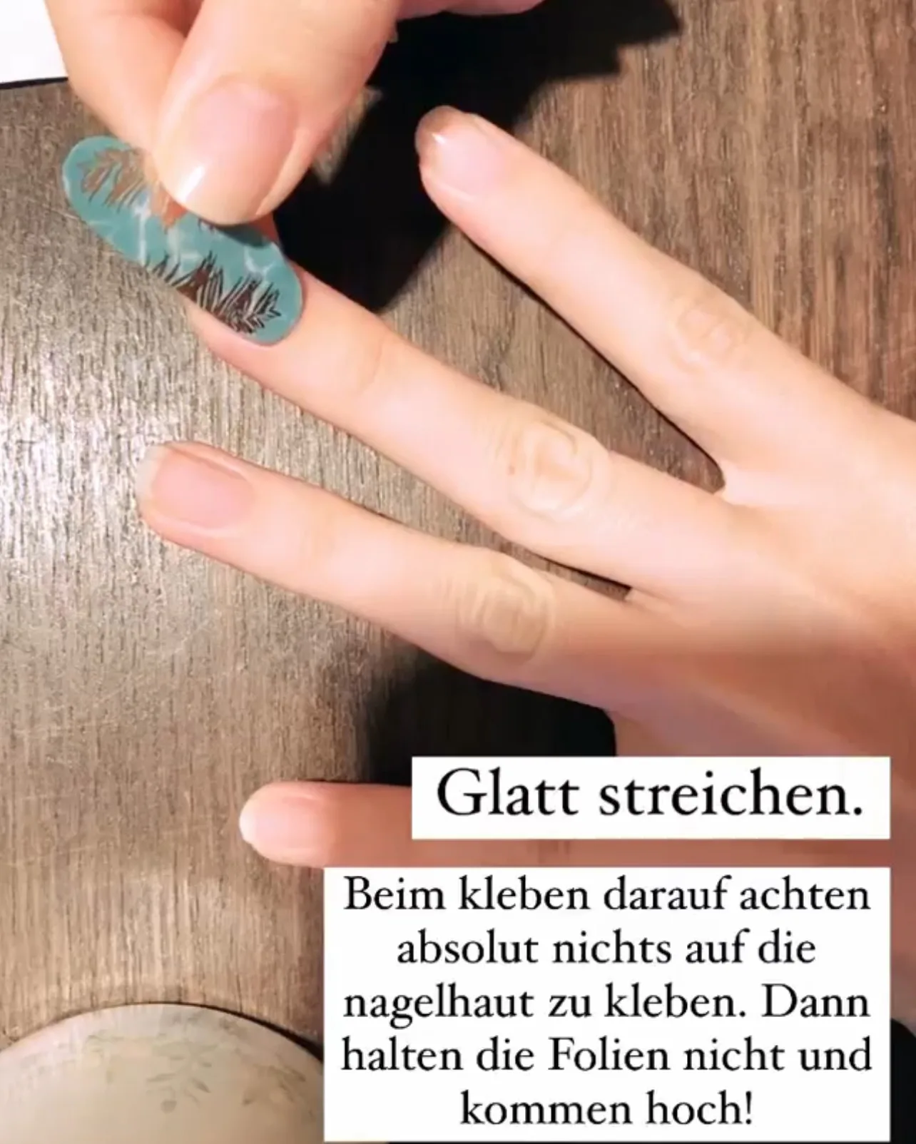 Türkise Nagelfolie wird mit dem Finger glatt auf den Nagel gestrichen