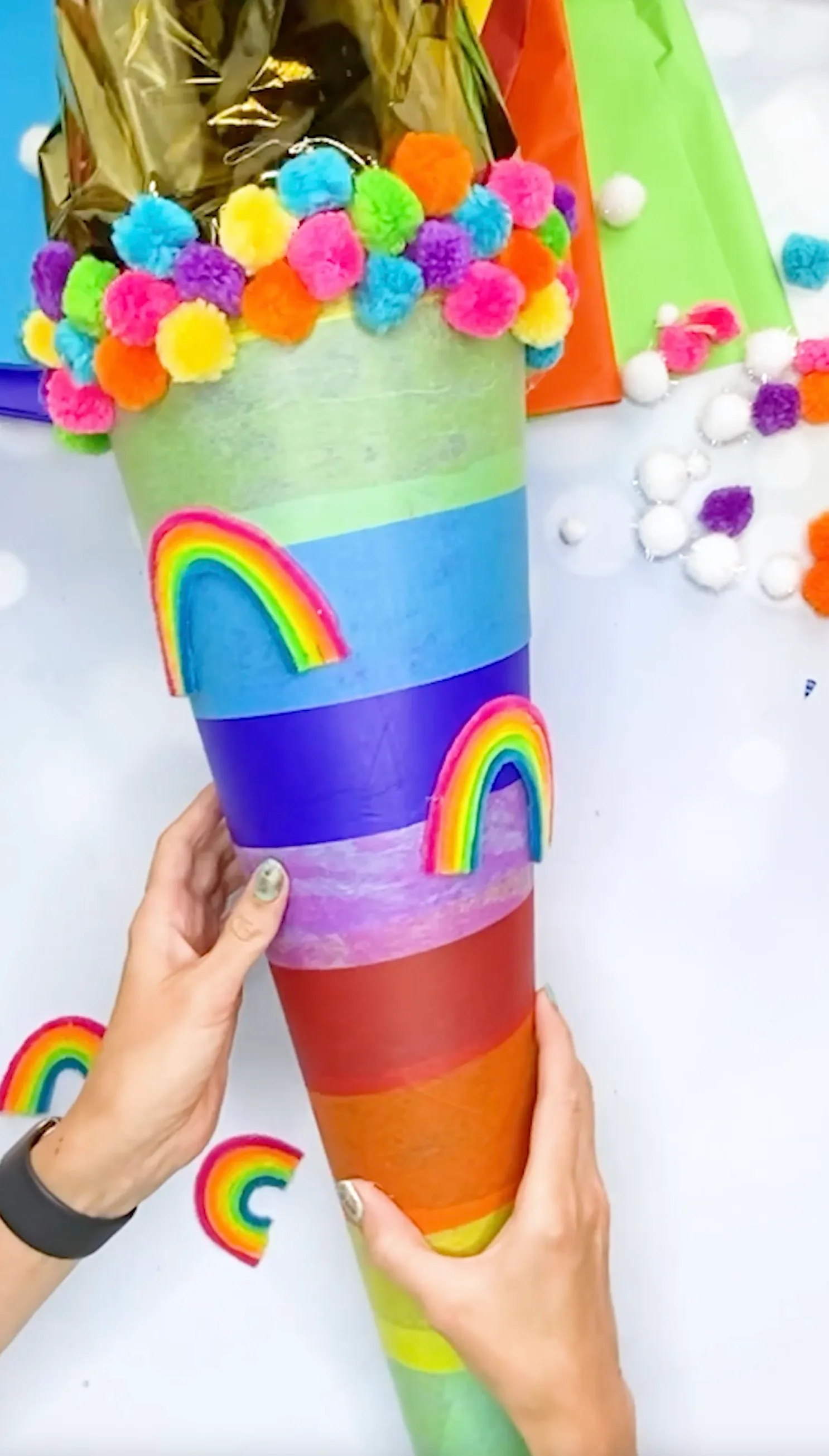 Kleine Regenbögen aus Chenilledraht werden auf die bunt gestreifte Schultüte geklebt