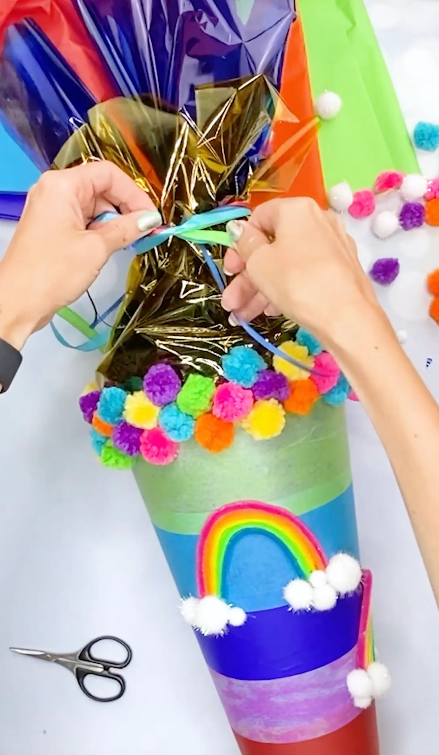 Die befüllte Regenbogen-Schultüte wird mit bunten Bändern über goldener Folie verschlossen