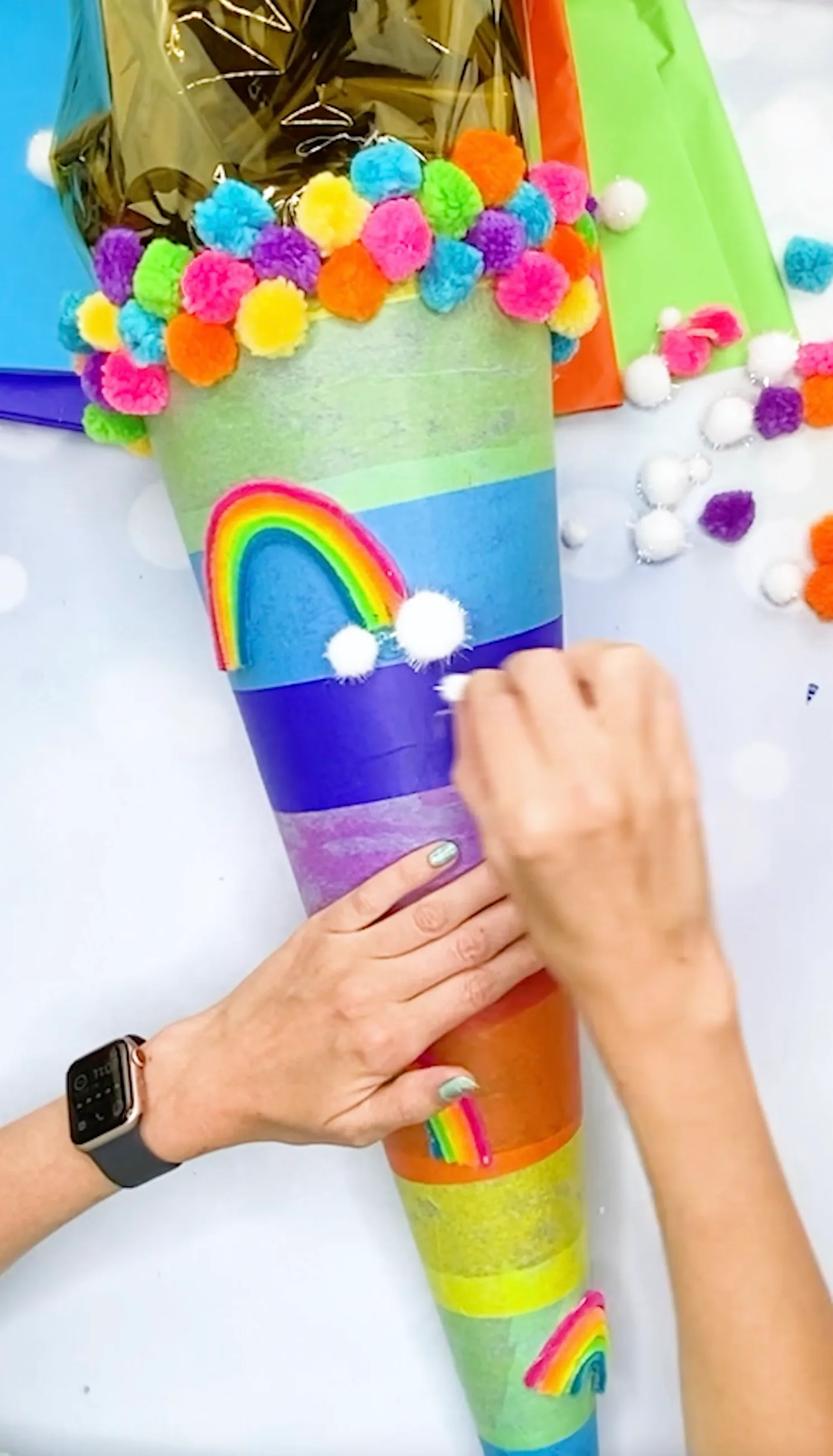 Weiße Pompons werden als Wolken unter dem Regenbogen auf die Schultüte geklebt