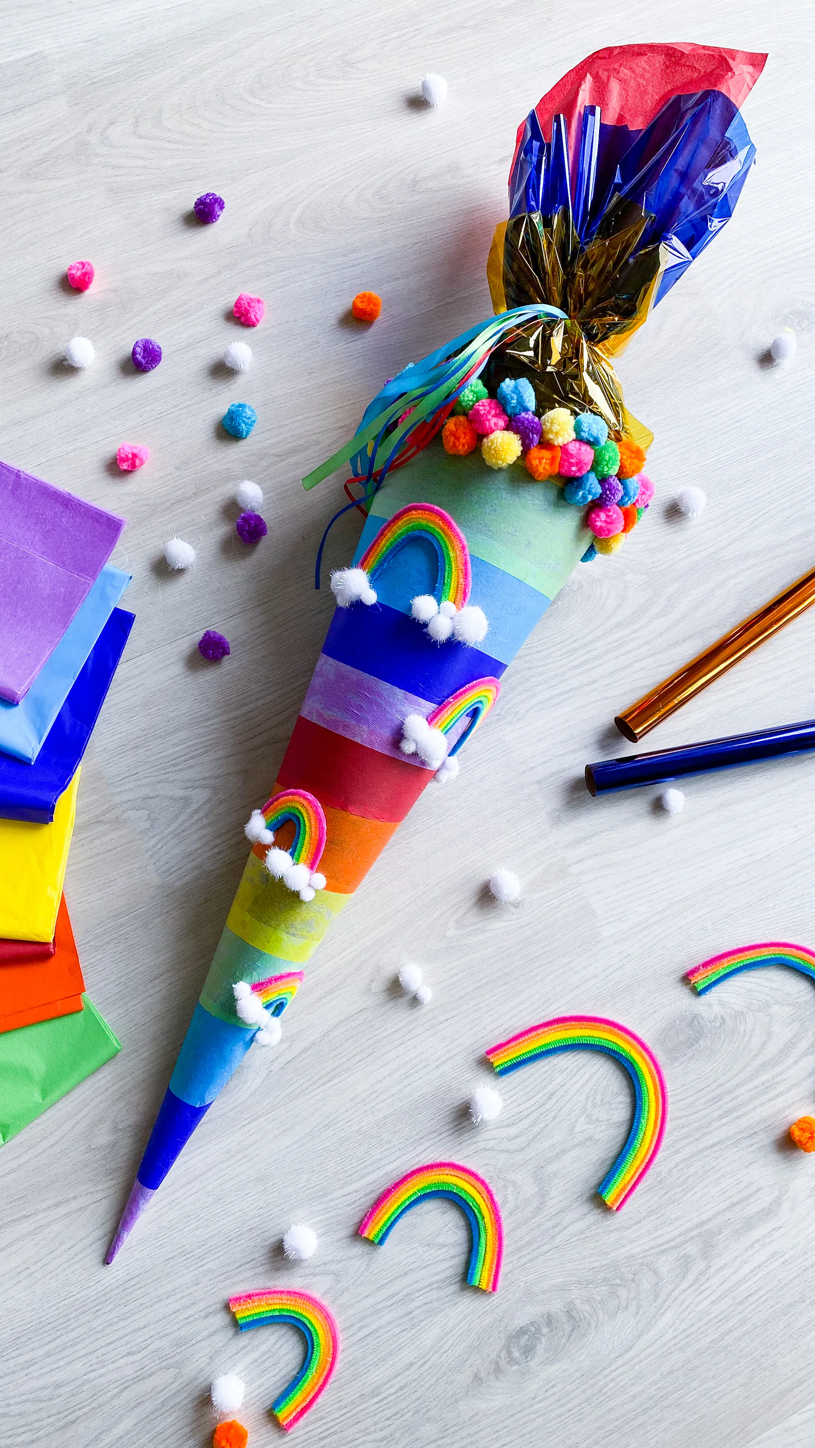 Fertige Regenbogen-Schultüte mit bunten Streifen, Pompons und kleinen Chenilledraht-Regenbögen