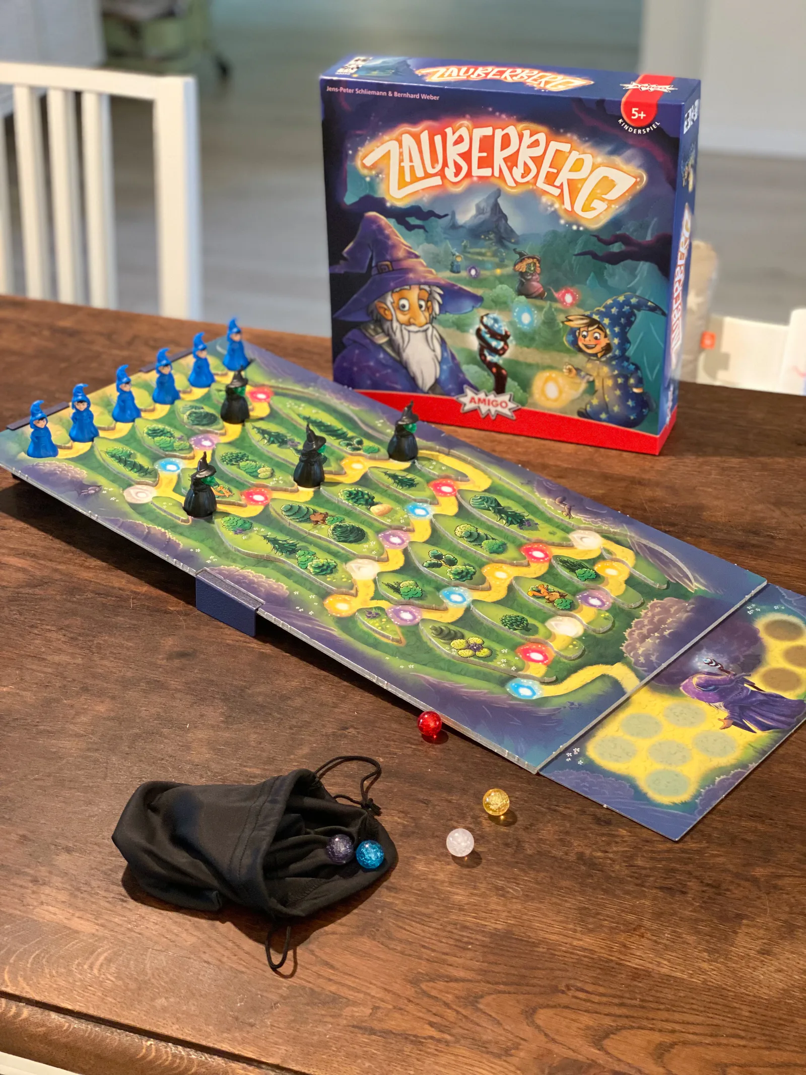 Spielschachtel und aufgebautes Zauberberg-Spielbrett mit blauen Zauberlehrlingen und schwarzen Hexen