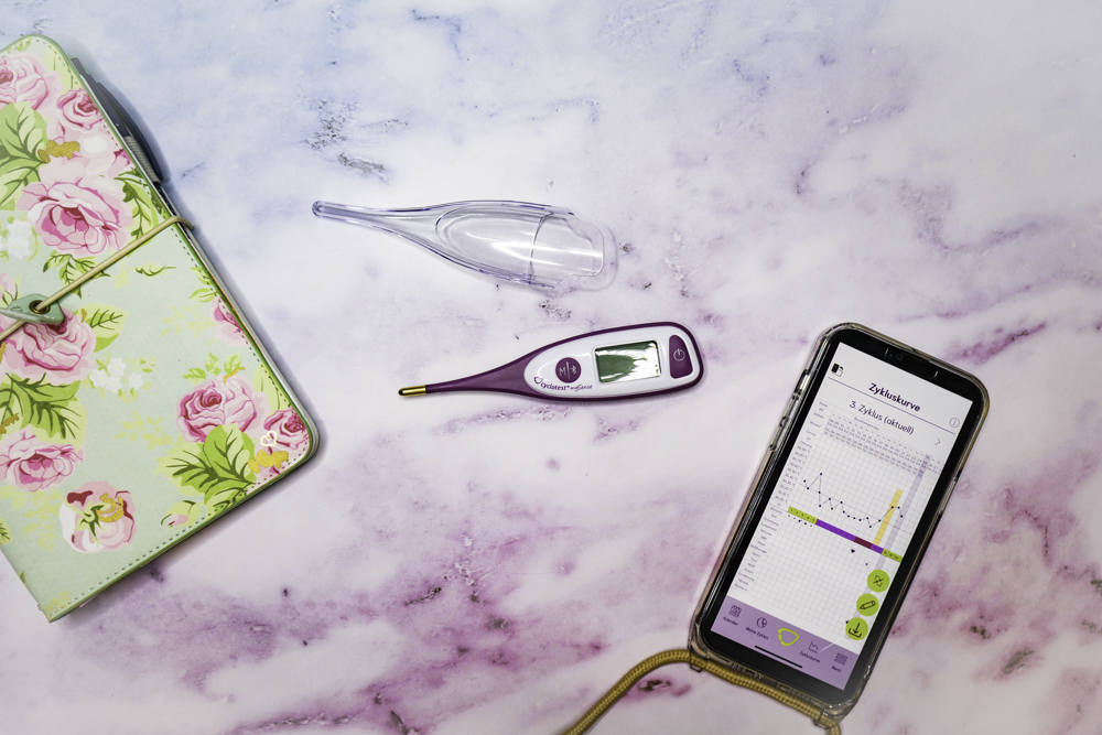 cyclotest mySense Basalthermometer neben einem Smartphone mit Zykluskurve