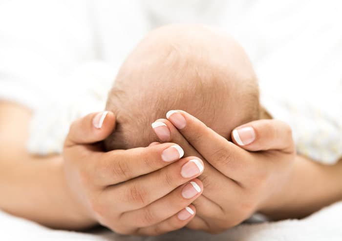 Eine Frau hält den Kopf eines Babys mit ihren Händen und bespricht dabei die Wahl des Geburtsortes.