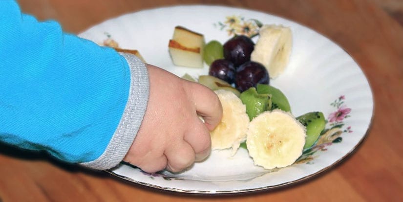 Die Hand eines Kindes auf einem Obstteller zeigt den unterhaltsamen Aspekt von BLW-Mahlzeiten (Baby Led Weaning).